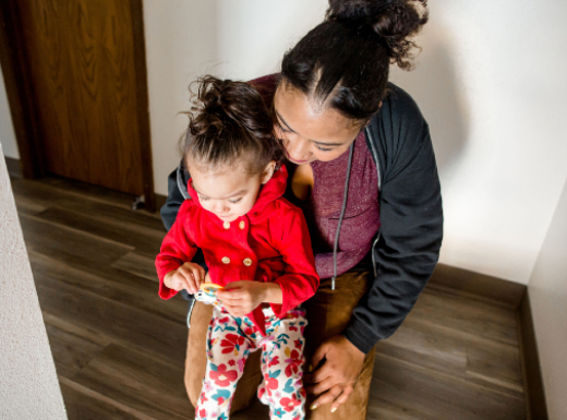 Mom holding daughter and daughter is playing with a toy